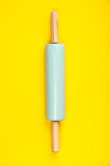 Blue rolling pin on yellow background, flat lay