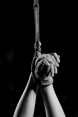 Hands of a victim tied up with rope hanging on ceiling