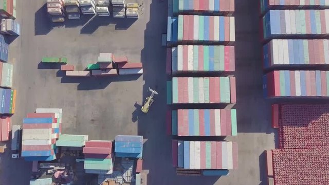 A container cargo carrier forklift machine moves through a large container yard while many truck wait to be loaded (4K)