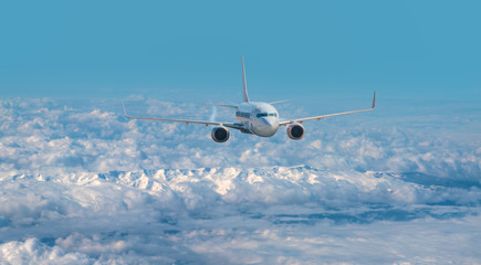 An airplane is flying over low clouds and city with blue sea - White commercial airplane flying over city