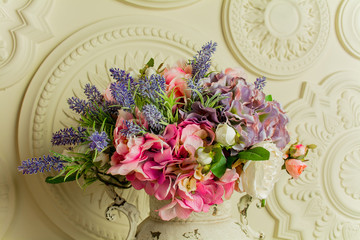 Flowers in a beige metal vase on the background of a beige wall with stucco. Provence style, neoclassical