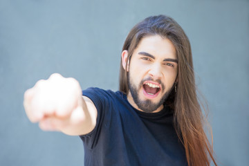 Excited shouting young man gesturing with fist clench. Rock band played with long hair doing fist bump. Greeting concept