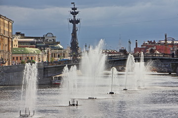 Fototapeta premium Russia, Moscow, Fountains on Vodootvodny canal, view from Bolotnaya square on background of monument to Great Peter and famous confectionery Red October on summer day against stormy sky