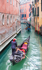 Venetian gondolier punting gondola through green canal waters of Venice Italy
