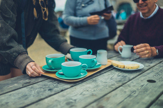 Young woman placing tray with cups on table