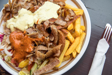 Dönerteller mit Kalb Fleisch, Knoblauch Soße, Scharf, Pommes und Salat an Dönerbude Holz Tisch
