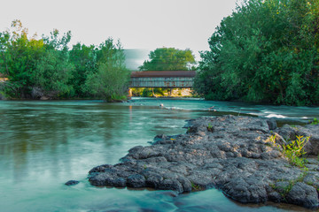 Long Exposure of Train Crossing Rusty Vandalized Bridge over River 