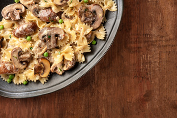 Mushroom and cheese pasta. Farfalle with cremini and green peas, top shot on a dark rustic wooden background with copy space