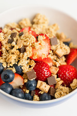 Healthy muesli or cereal breakfast bowl with granola made of toasted rolled oats, organic honey, milk chocolate chips and tiny graham cracker cookies served with fresh strawberries and blueberries