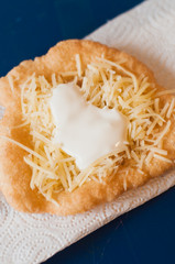 Traditional street food from Hungary or Poland called Langos or Hungarian Pizza, deep fried flat bread made of yeast dough with grated cheese, garlic oil, hot sauce like sriracha and sour cream
