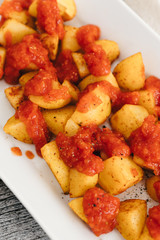 Papas Bravas, deep fried potato cubes typically served as tapas in Madrid, Spain with spicy mojo rojo, a red hot sauce made of tomatoes, bell peppers, onions and chili on white plate and wooden table