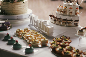 Delicious candy bar at wedding reception. White and chocolate desserts with fruits,  cupcakes on stand, modern sweet table at wedding or baby shower. Luxury catering concept
