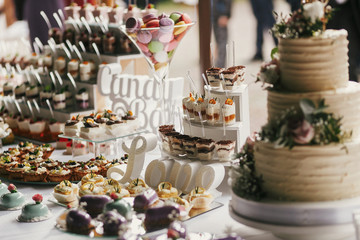 Delicious candy bar at wedding reception. White and chocolate desserts with fruits, macarons, cake,...
