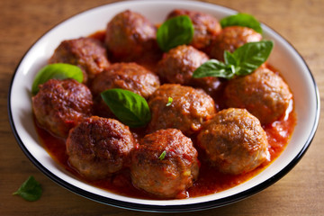 Meatballs in tomato sauce, garnished with basil in bowl on wooden table