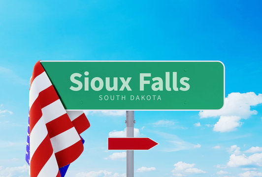 Sioux Falls – South Dakota. Road Or Town Sign. Flag Of The United States. Blue Sky. Red Arrow Shows The Direction In The City