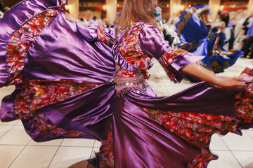 Beautiful gypsy girls dancing in traditional purple floral dress at wedding reception in restaurant. Woman performing romany dance and folk songs in national clothing. Roma gypsy festival