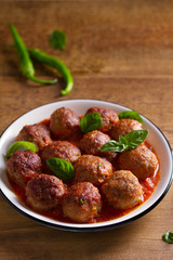 Meatballs in tomato sauce, garnished with basil in bowl on wooden table