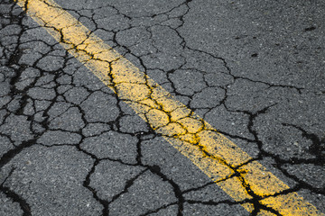 Cracked asphalt road with yellow dividing line