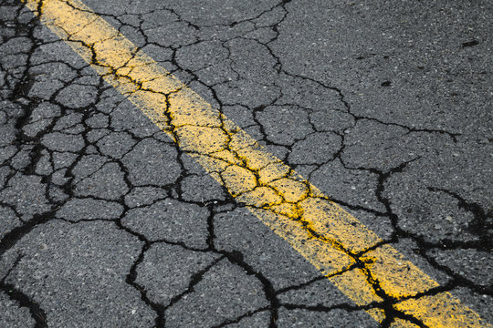 Cracked asphalt road with yellow dividing line