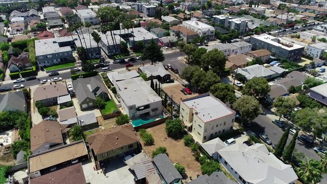 Pan down in to flying drone shot over Los Angeles neighborhood with rooftops, cars on the road, swimming pools and people about their day. 4k