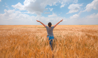 Naklejka na ściany i meble Woman in a golden wheat field at amazing cloudy sky