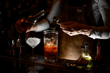 Professional male bartender pouring an alcohol from the steel jigger to the measuring glass cup