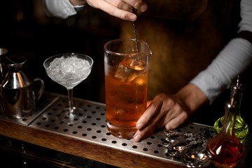 Bartender stirring a delicious brown cocktail in the measuring glass cup