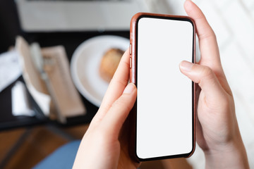 Mockup image of a woman holding mobile phone with blank black screen in modern loft cafe