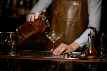 Bartender pouring an alcoholic drink from the measuring cup to the cocktail glass
