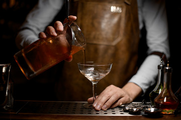 Bartender pouring an alcoholic drink from the measuring cup to the empty cocktail glass