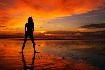 sunset with the silhouette of a model with  reflection  on the beach in bali 