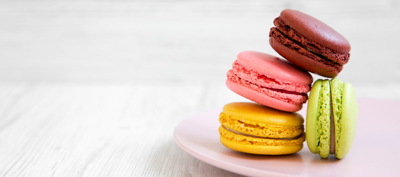 Sweet and colorful macarons on a pink plate over white wooden background, side view. Copy space.