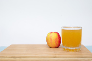 glass of apple juice and apple on wooden table on white background