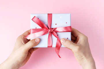 Male hands holding gift box with ribbon on pink background, top view