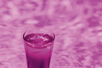 Coctail with ice in the glass on the swimming pool background.