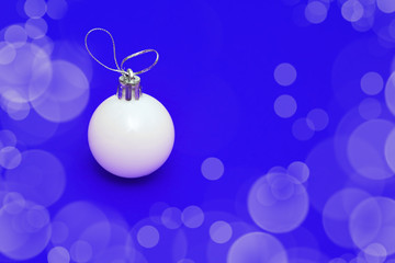 Fototapeta na wymiar Christmas glass ball on blue paper background. New Year eve decoration. Winter Holiday background with copy space and shiny bokeh.