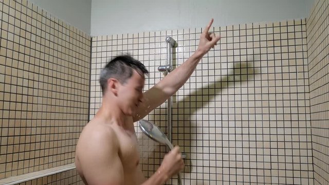 Portrait of young man singing emotionally in the shower using the shower head with flowing water instead of a microphone. Guy washes, sings and dances in the shower.