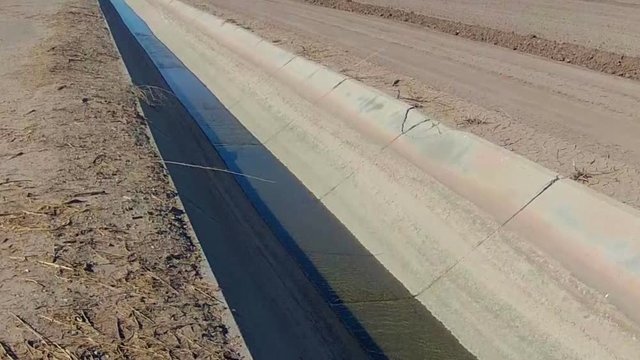 Dry Barren Farm Fields With Low Water Trickling In Irrigation Canal