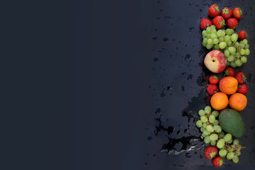 fresh juicy strawberries, grapes, peaches, apricots, avocados on a black wet background in splashes and drops of water, top view