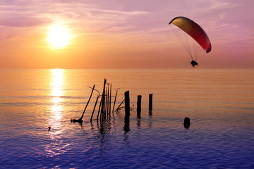 colored parachute flies in the sky against the background of the remains of a sunken destroyed ship in shallow water at sunset, travel, flight, vacation Concept