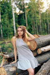Naklejka na ściany i meble beautiful girl in a gray dress on the background of logs in the forest