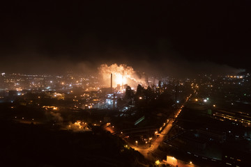 Aerial view of steel plant at night with smokestacks and fire blazing out of the pipe; industrial...