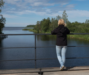 Fototapeta premium A girl stands on a bridge and looks into the distance. The river flows into the lake. Spring. Sunny day.