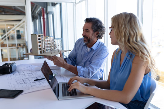 Male and female architect discussing over architectural model at table in a modern office