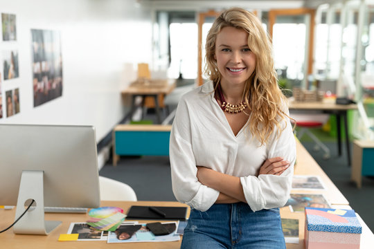 Female graphic designer with arms crossed sitting at desk in a modern office