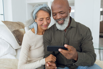 Couple sitting on a couch inside a room while looking at smartphone