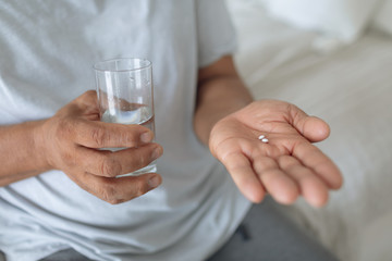 Man sitting on the bed while holding pills and a glass of water