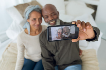 Couple sitting on a couch inside a room while taking picture with smartphone