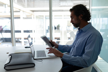 Fototapeta na wymiar Businessman working on digital tablet and laptop at desk in office