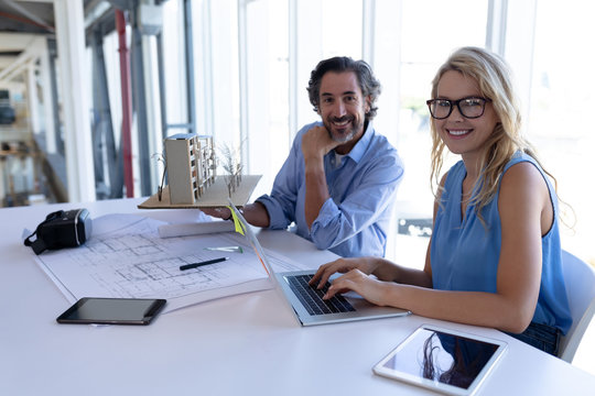 Male and female architect looking at camera while working table in a modern office